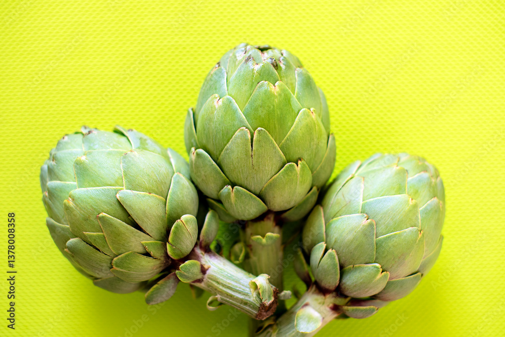 Fototapeta premium Three fresh artichokes resting on a vibrant yellow surface, showcasing their natural texture and intricate patterns. A vivid presentation of vegetables, perfect for healthy eating or cooking themes.