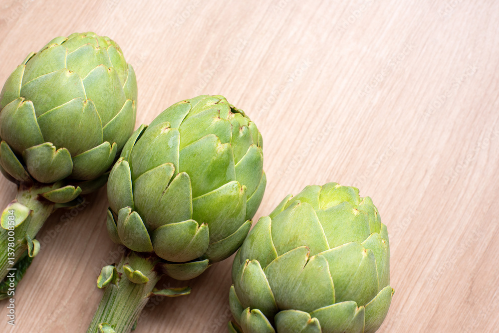 Three vibrant green artichokes are aligned against a natural woodgrain surface, showcasing their fresh and symmetrical appeal for culinary or artistic contexts. Cooking ingredients, healthy food Three vibrant green artichokes are aligned against a natural woodgrain surface, showcasing their fresh and symmetrical appeal for culinary or artistic contexts. Cooking ingredients, healthy food