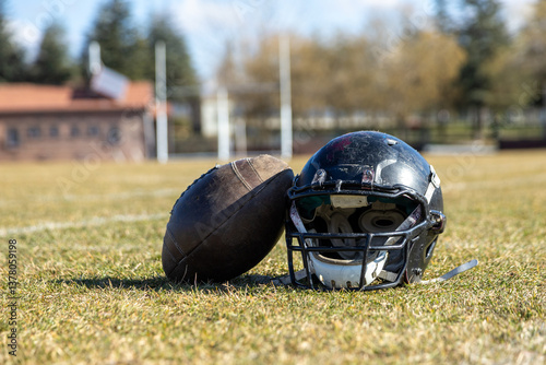 worn helmet and american football ball, worn american football helmet and football field, grass and white lines, black helmet