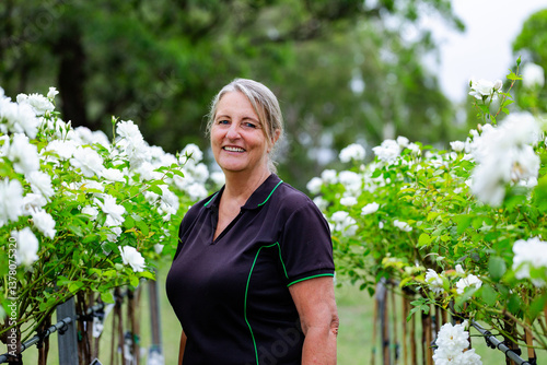 Portrait of female horticulturalist standing amongst white roses in nursery garden photo