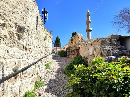 Fototapeta Naklejka Na Ścianę i Meble -  Photo of a scenic cobblestone street (Kalderimi) leading to the Medieval Clock Tower of Rhodes, Greece, built in 1852 and still operational today, offering great panoramic view of the city.
