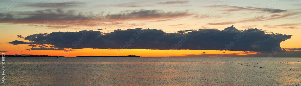 Long big dark cloud over the sea at sunset
