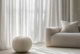 Minimalist living room with soft furnishings.  Sunlight streams through sheer curtains illuminating a modern space featuring a textured ottoman and a sculpted sofa