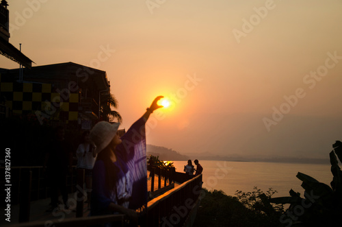 Asian thai woman traveler posing catching the sun for take photo at riverside of Mae Khong river in sunset time at Chiang Khan