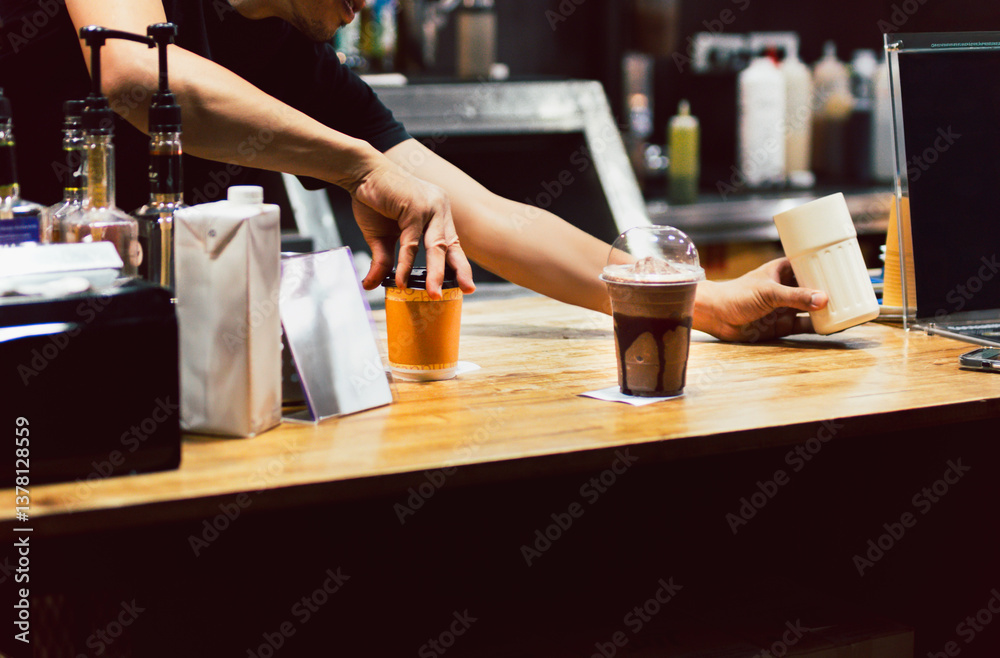 Shot in low light of barista serving a fresh coffee in cafe. Shot in low light of barista serving a fresh coffee in cafe.