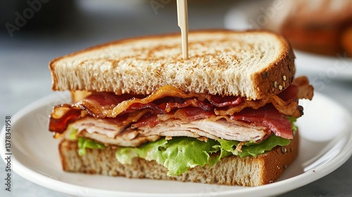 A turkey sandwich with bacon and lettuce is on a white plate. The sandwich is cut in half and has a toothpick holding it together