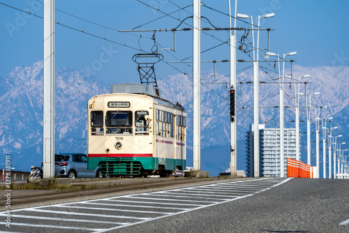 立山連峰を背景に富山大橋を渡る富山地方鉄道の市内電車