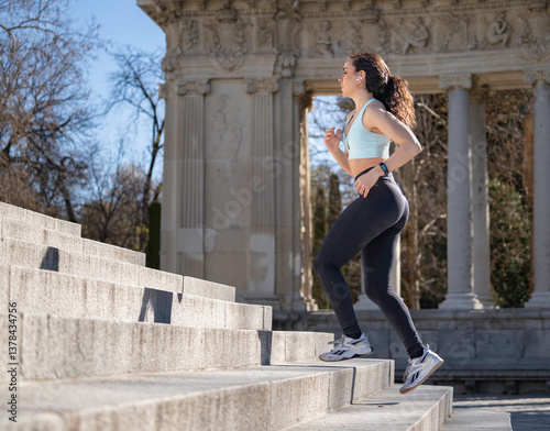 Fit woman running up stairs and listening music with earphones in a park photo