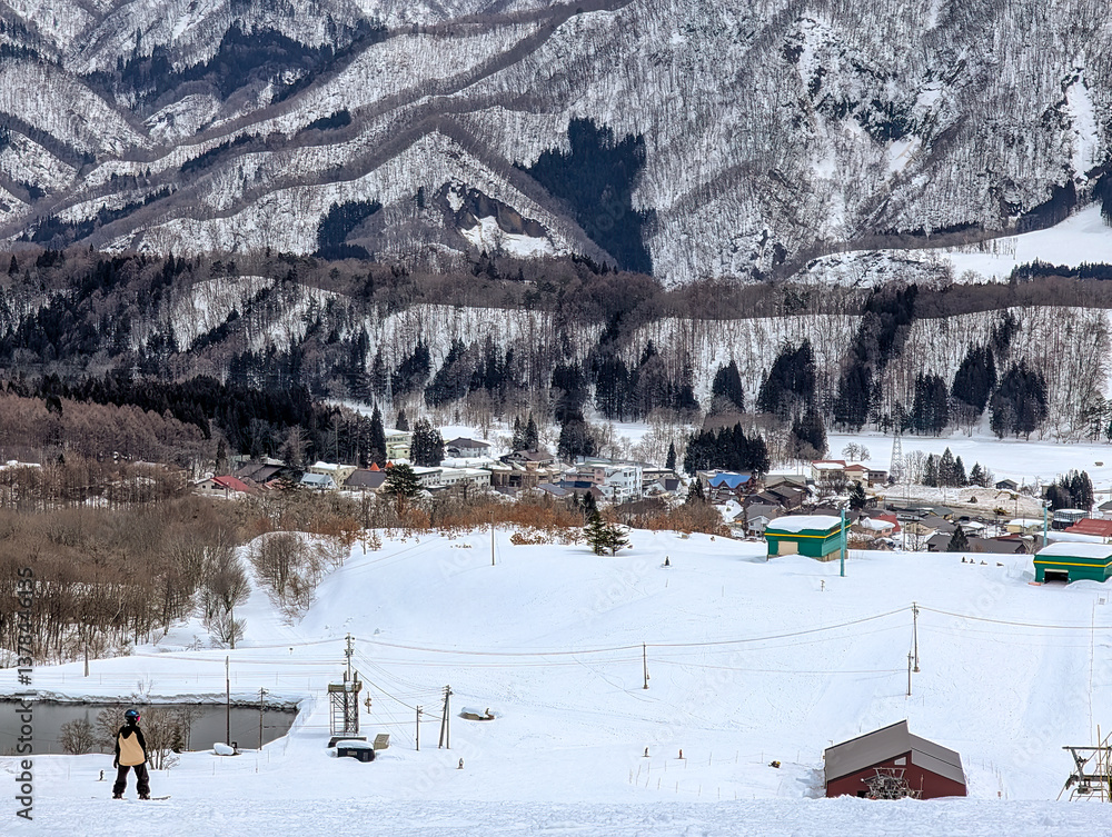 Snowboarder at top of a ski slope with mountain background on a cloudy day
