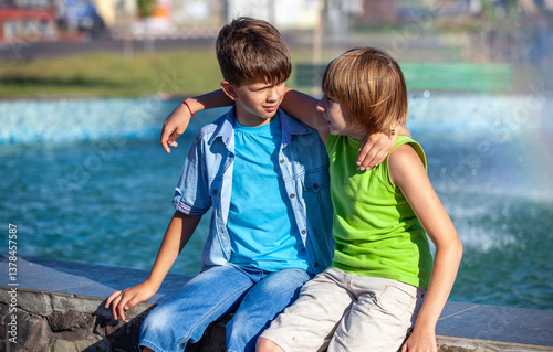 Two boys are sitting on a wall next to a fountain