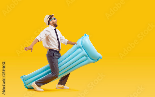 Happy funny cheerful overjoyed business man in office shirt, tie, trousers, and sun hat riding on blue water mattress and running isolated on yellow color background. Summer holiday, vacation concept