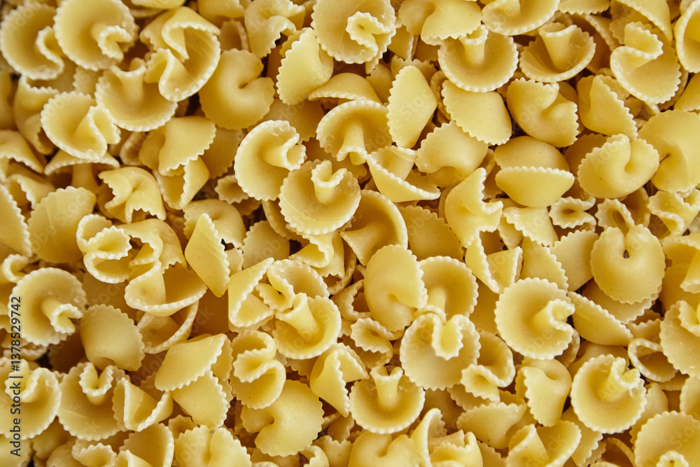 Close-up view of uncooked funghetti pasta showing curled, mushroom-like shapes with ridged edges, forming a textured background in golden yellow tone. Close-up view of uncooked funghetti pasta showing curled, mushroom-like shapes with ridged edges, forming a textured background in golden yellow tone.