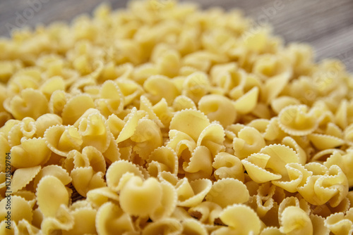 Side view of uncooked funghetti pasta with curled, ridged shapes in shallow depth of field, creating a soft textured background in warm golden tones