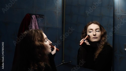 The girl in the video is doing her makeup in the bathroom. In the reflection of the mirror we see that she is now applying powder to her face with a special brush.