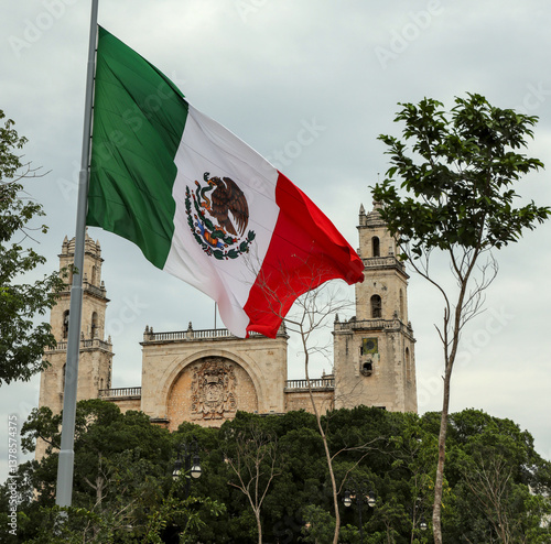 Mexico flag flying in wind at plaza grande (Merida, Yucatan peninsula) Mexican heritage state capital (famous tourist cathedral church background) colonial catholic travel tourism destination mayan