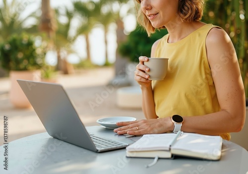 Businesswoman drinking coffee and using laptop at outdoor cafe in tropical resort, combining work and leisure