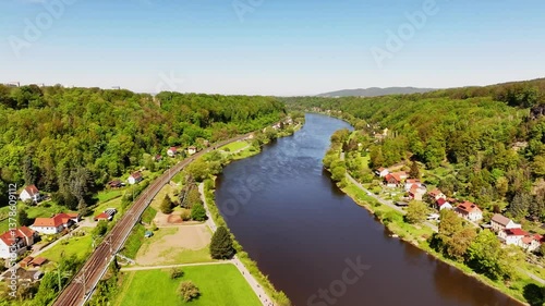 A drone flies through the Elbe Valley in Saxon Switzerland on a sunny day, capturing scenic views of small houses, a railway track, and the stunning natural landscape. Drone move forward