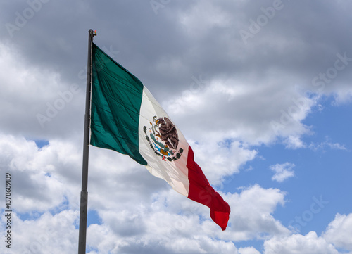 mexican red green and white flag flying in the breeze against a blue cloudy sky background (banner bandera large flagpole) patrimony pride patriotism nation country state