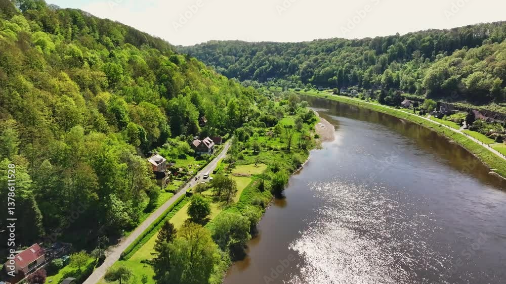 A drone flies through the Elbe Valley in Saxon Switzerland on a sunny day, capturing scenic views of small houses, a railway track, and the stunning natural landscape. Drone move forward A drone flies through the Elbe Valley in Saxon Switzerland on a sunny day, capturing scenic views of small houses, a railway track, and the stunning natural landscape. Drone move forward