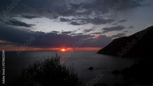 Obraz na płótnie beautiful scenic epic drone flight over the sea at sunset with the red sun setting into the sea on the horizon with a colorful sky full of gray clouds in Framura Italy Liguria landscape w salonie