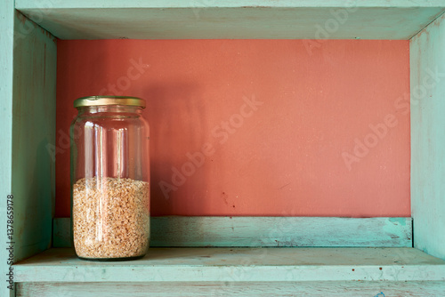 Wooden shelf displaying glass jar overflowing with oatmeal, creating warm kitchen atmosphere with rustic pantry charm