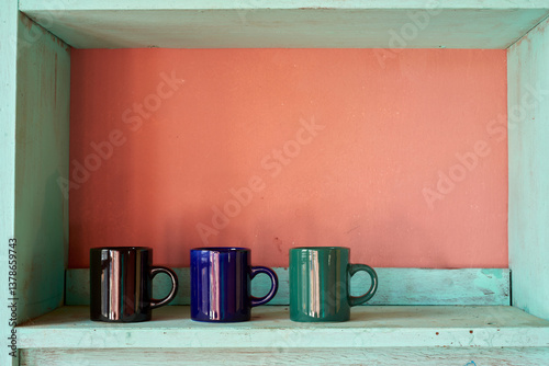 Ceramic mugs on turquoise bookshelf, complementing soft coral wall with warm, nostalgic styling