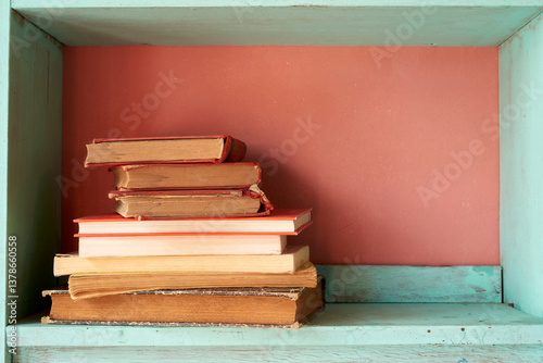 Vintage red books stacked on light green wooden shelf, coral wall background, nostalgic reading nook with soft textural elements
