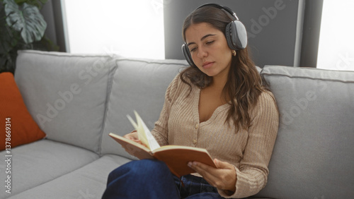 Obraz na płótnie Woman reading book while listening to music in cozy living room setting with headphones, showcasing a relaxed indoor environment. w salonie