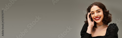 Radiant young woman with braces and striking red lips in elegant pose on grey backdrop