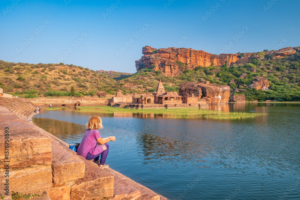 Woman exploring ancient ruins at Badami. Tourist sitting on lake shore relaxing at Badami temple, Karnataka, India