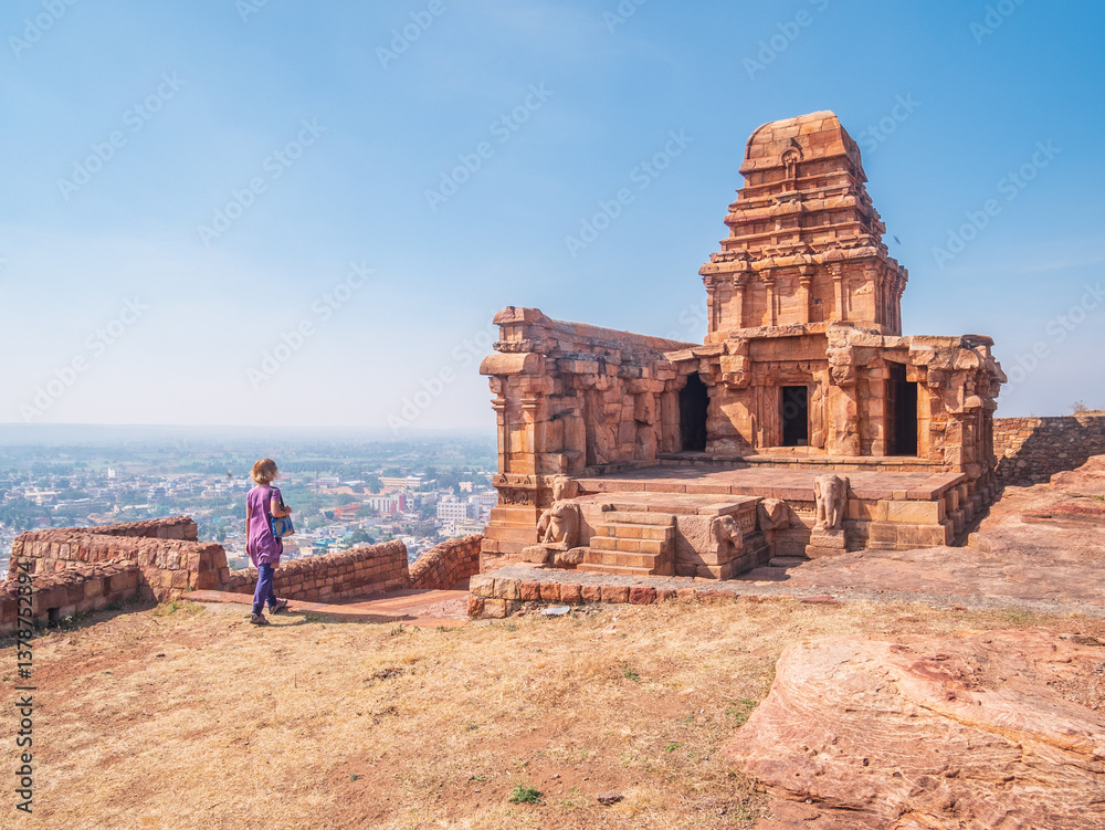 Woman exploring ancient temple site at Badami. Tourist walking among ruins stone walls gateways in Karnataka, India