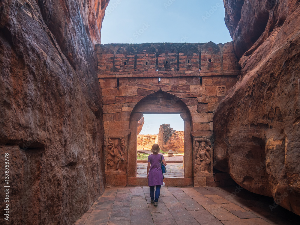 Woman exploring ancient temple site at Badami. Tourist walking among ruins stone walls gateways in Karnataka, India