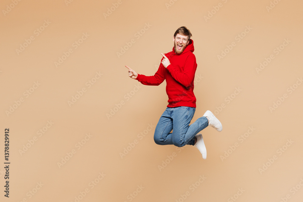 Full body side view young man he wear red hoodie casual clothes jump high point index finger aside on area mock up isolated on pastel plain light beige background studio portrait. Lifestyle concept. Full body side view young man he wear red hoodie casual clothes jump high point index finger aside on area mock up isolated on pastel plain light beige background studio portrait. Lifestyle concept.