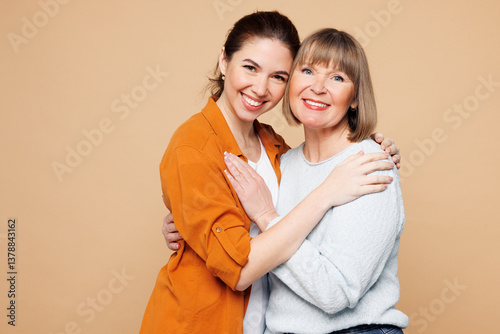 Elder smiling parent mom 50s years old with young adult daughter two women together wear casual clothes hug embrace looking camera isolated on plain pastel light beige background. Family day concept. photo