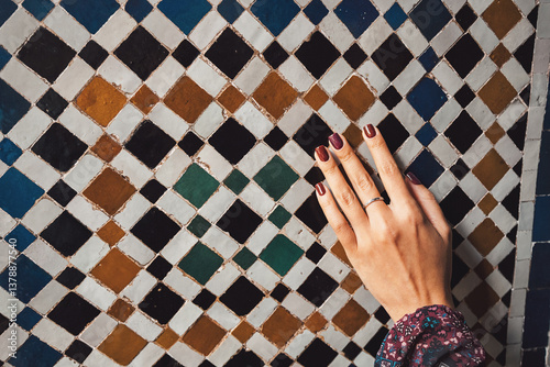 Obraz na płótnie Woman's hand with dark nail polish gently touching an ornate wall covered in traditional moroccan zellige mosaic tiles w salonie