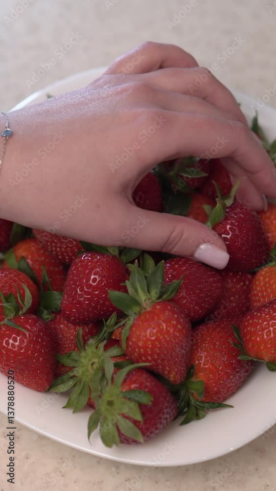 hand takes strawberries from a plate