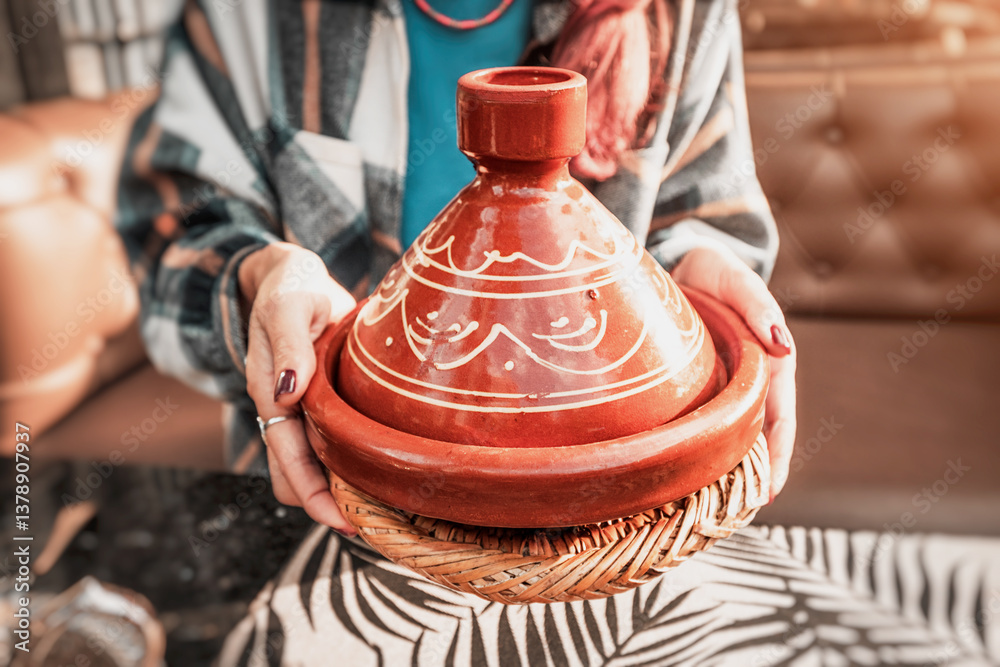 Close up of a woman's hands presenting a terracotta tajine, showcasing Moroccan culinary tradition