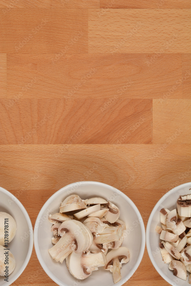 Three bowls with mushrooms, ranging from whole to finely chopped, on a wooden surface, shot from above Three bowls with mushrooms, ranging from whole to finely chopped, on a wooden surface, shot from above