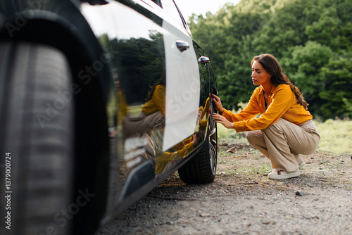 Φωτογραφία Young woman broken down on country road, sitting near rear wheel and checking ca