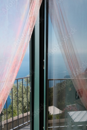 Wallpaper Mural Soft sunlight filters through sheer curtains of a hotel room on the Amalfi Coast, revealing a balcony view of the blue sky, distant ocean, and serene morning horizon. Torontodigital.ca