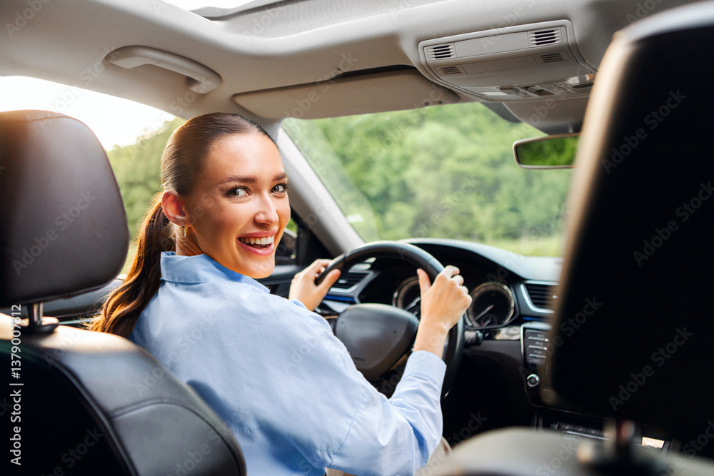 Excited European lady driving car, sitting on drivers seat and smiling, holding steering wheel looking back, view from back seat Excited European lady driving car, sitting on drivers seat and smiling, holding steering wheel looking back, view from back seat