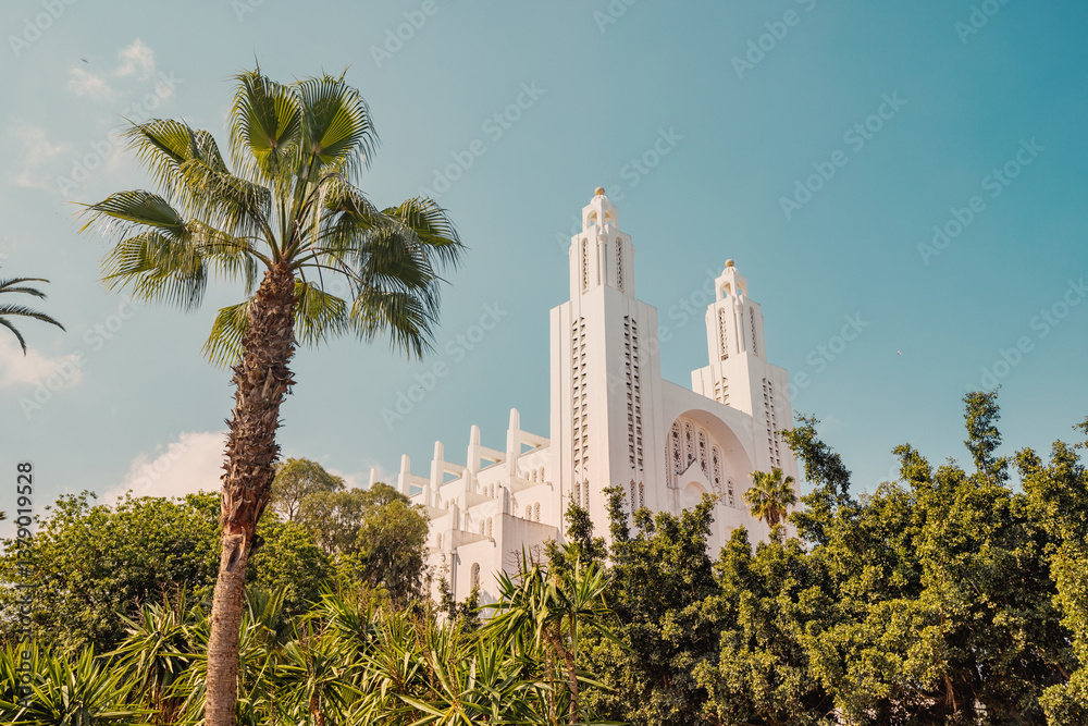 Sacred Heart Cathedral of Casablanca with its white facade and two towers, surrounded by palm trees and green vegetation