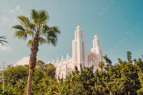 Obraz na płótnie Sacred Heart Cathedral of Casablanca with its white facade and two towers, surrounded by palm trees and green vegetation w salonie