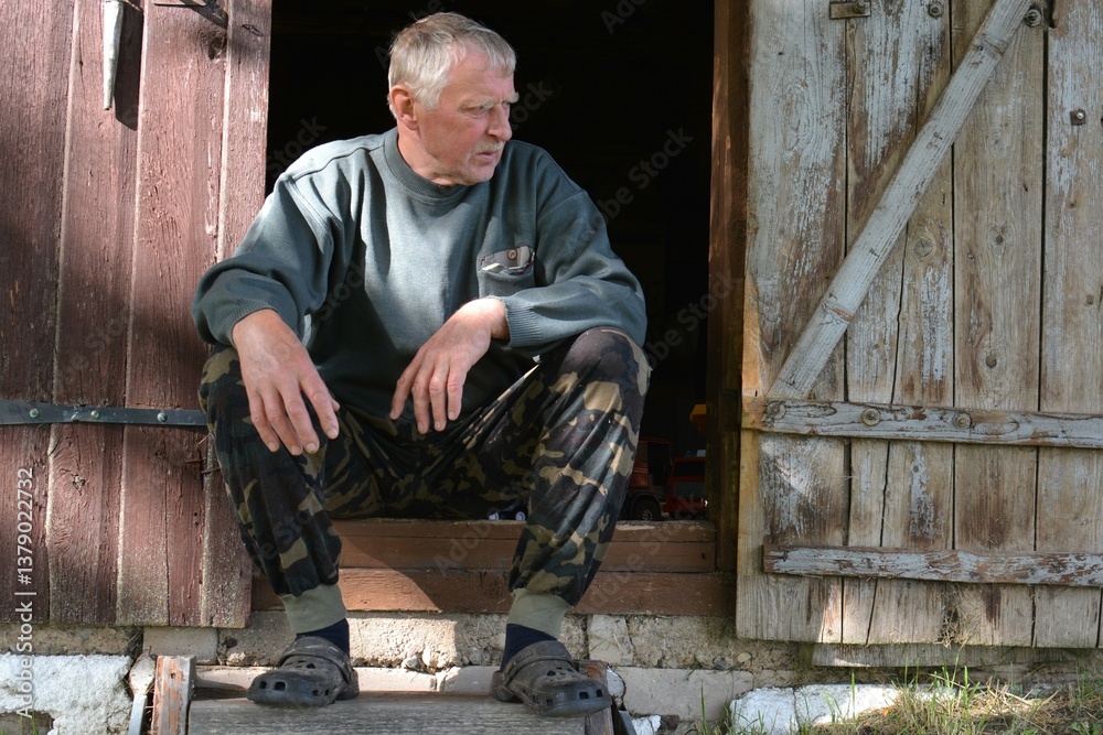 Older man sitting on open barn stairs in village. Senior man spending time in rural area outside. Older man sitting on open barn stairs in village. Senior man spending time in rural area outside.