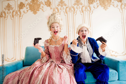 Картината върху платно Amused couple in vintage costumes playing video games together on a luxurious an