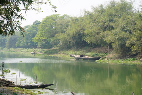 A tranquil river scene, likely in a rural area with several small wooden boats moore along the banks and in the water