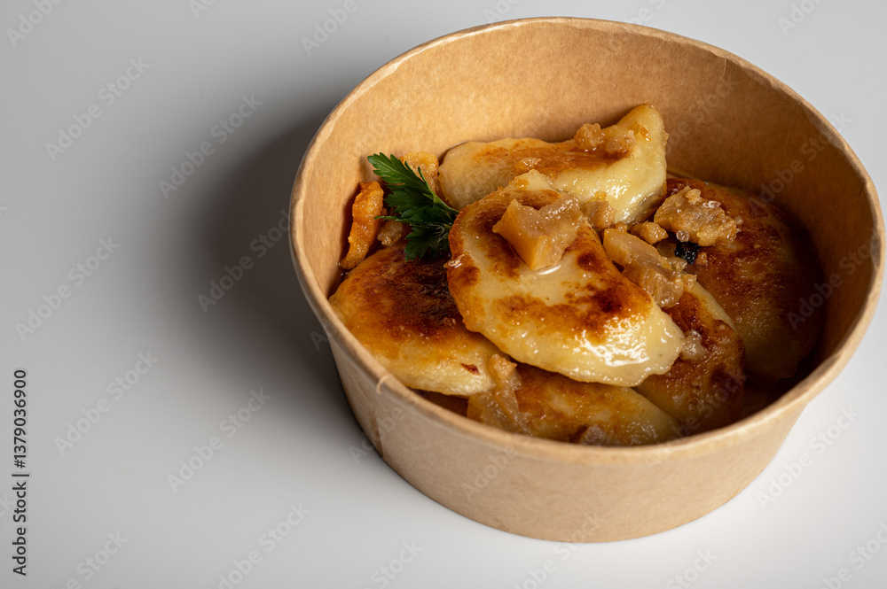 Fried dumplings with golden crust and crispy pork cracklings in a kraft paper bowl. Traditional Eastern European food, close-up, delicious street food concept