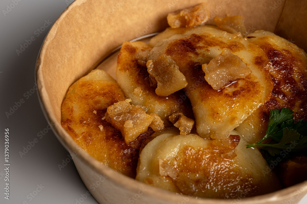 Fried dumplings with golden crust and crispy pork cracklings in a kraft paper bowl. Traditional Eastern European food, close-up, delicious street food concept