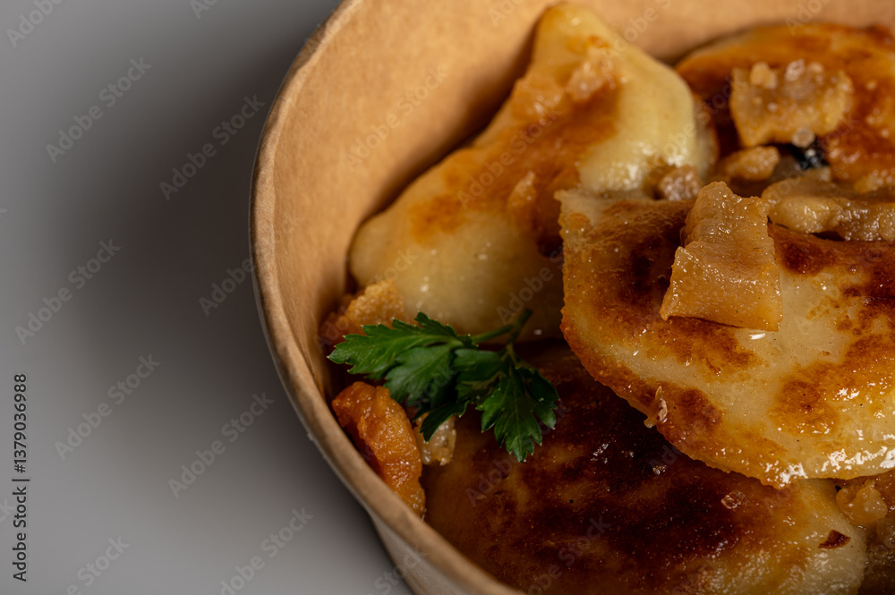 Fried dumplings with golden crust and crispy pork cracklings in a kraft paper bowl. Traditional Eastern European food, close-up, delicious street food concept