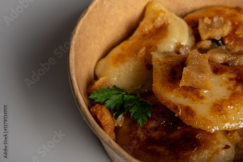 Obraz na płótnie Fried dumplings with golden crust and crispy pork cracklings in a kraft paper bowl. Traditional Eastern European food, close-up, delicious street food concept w salonie